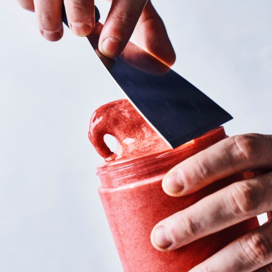 Une photographie macro montrant des mains manipulant une spatule en acier pour retirer l'excédent d'un pot de glace